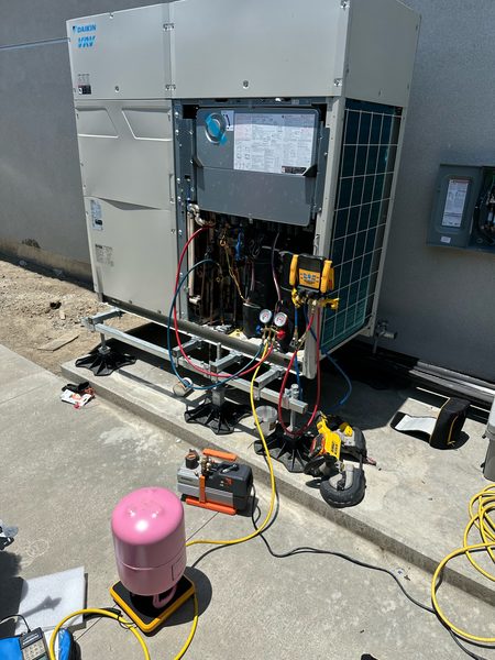 Technician starting up a Daikin VRV unit with gauges and a vacuum pump